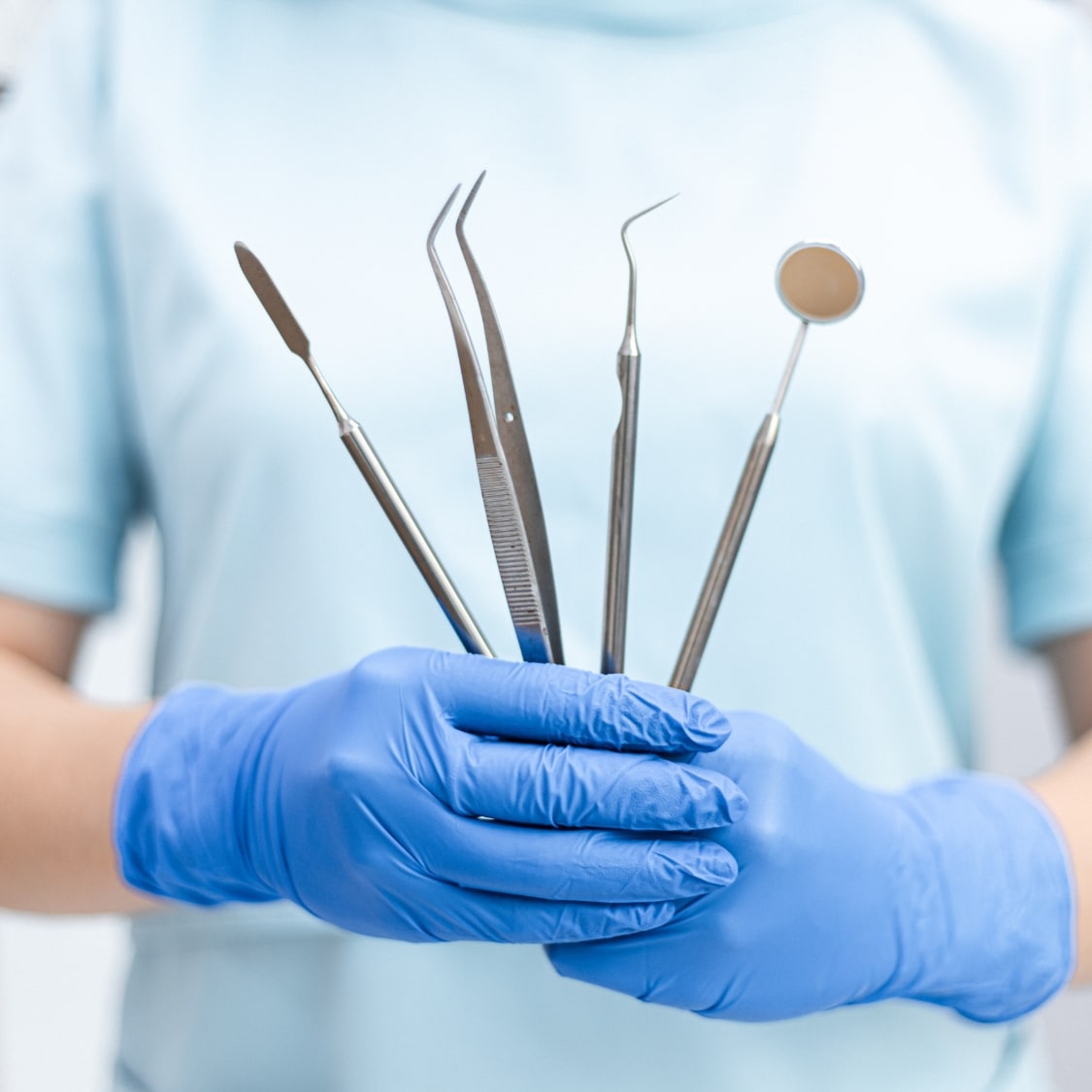 Zahnmedizinisches Fachpersonal in hellblauer Kleidung hält mit blauen Einweghandschuhen verschiedene zahnärztliche Instrumente – Symbolbild für professionelle Ausstattung und Präzision in der Praxis für Zahnerhaltung Dr. Michaela Strumpski, Halle (Saale). Dieses Bild steht im Zusammenhang mit der Mitarbeitersuche der Praxis. Es vermittelt einen Eindruck vom Arbeitsumfeld und der täglichen Praxisroutine – modern, hygienisch und professionell. Ideal für den Einsatz auf Karriereseiten oder in Stellenausschreibungen.