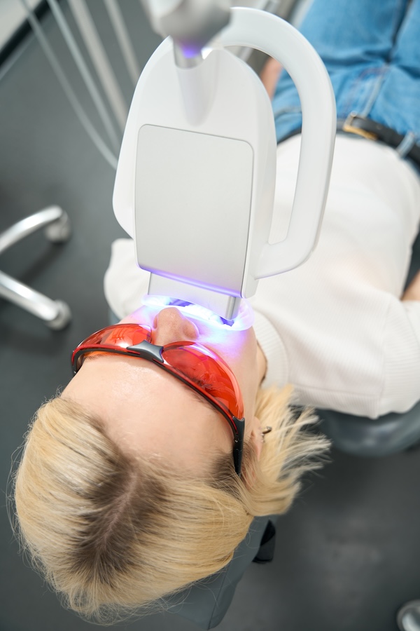Frau mit Schutzbrille bei einer professionellen Zahnaufhellung unter Bleaching-Lampe. Zahnerhaltung Halle – Zahnarztpraxis Dr. Michaela Strumpski für ästhetische Zahnmedizin.